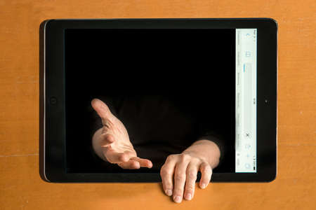 An illustration of a man's hands coming out of an iPad on a brown tableの写真素材