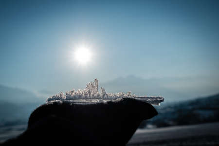 A hand holding ice under the sunlight with mountains on the blurry backgroundの写真素材
