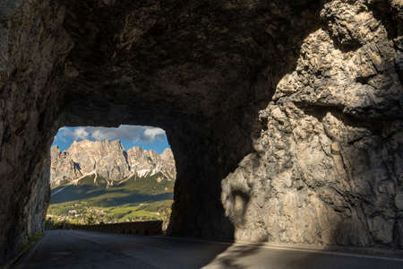 A road covered by rocks surrounded by hills and dolomites under the sunlight in Italyの写真素材