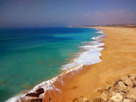 An aerial shot of a sandy shore during sunny weather in CÃ¡diz, Spain.