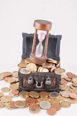 A vertical shot of a small treasure box with an hourglass placed at the top of the coins with a white color in the backgroundの写真素材