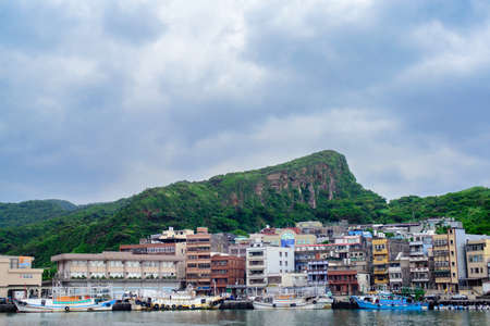A beautiful shot of apartment buildings and boats on the shore near high grassy hills in Yehliu,...