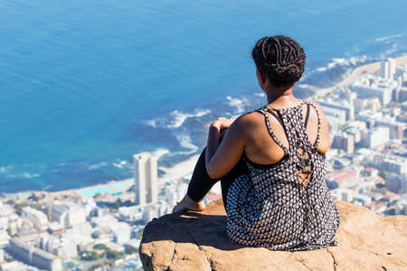 CAPE TOWN, SOUTH AFRICA - Dec 27, 2019: An African women sits on a cliff on at the top of Lion's head mountain. This is a popular tourist attraction in the city.のeditorial素材