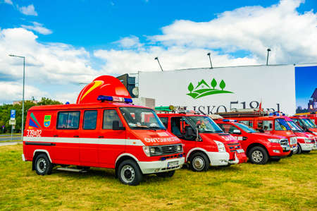 POZNAN, POLAND - Aug 03, 2019: Row of parked red fire vans on green grass field during a fire...