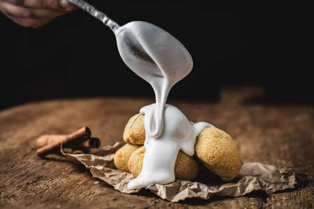 A closeup shot of a spoon dripping shite cream over cookies