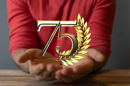 The golden number 75 and a spike of wheat over someone's hand