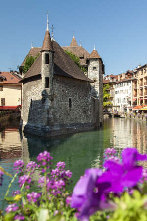 A vertical shot of the Le Palais de I'lle with purple flowers in the foreground in Annecy, Franceのeditorial素材