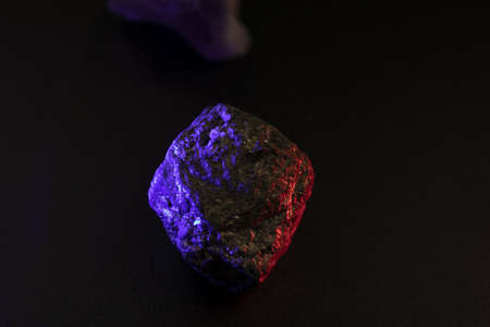 A closeup shot of a mineral stone with purple and red color tint against a black background