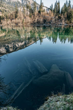 A vertical picture of a lake surrounded by rocks and forests with trees reflecting on the water