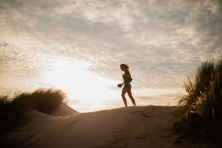 A low angle shot of the silhouette of a woman walking on sand during sunsetの写真素材