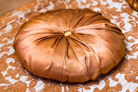 A decorative round-shaped cushion on a fabric with floral patterns