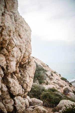 A vertical shot of a cliff in front of the water under a clouded skyの写真素材