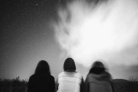 A low angle shot of three friends stargazing under cloudy skiesの写真素材