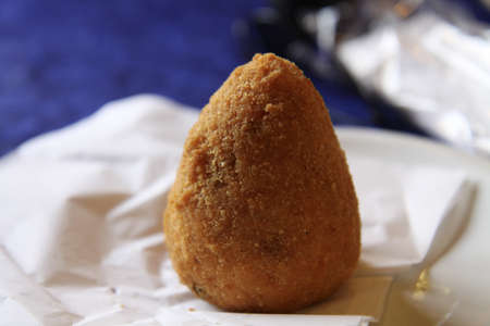 A closeup of a big arancini ball in a plate under the light with a blurry background