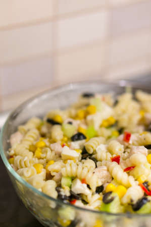 A vertical shot of macaroni mixed with vegetables in a glass bowlの写真素材