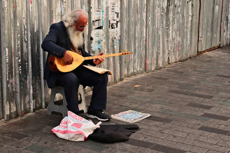 ISTANBUL, TURKEY - Sep 16, 2019: An old bearded man playing music on a traditional Turkish guitar on the sidewalk.のeditorial素材