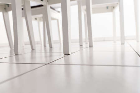 white chair legs under a kitchen table on a tiled floor in soft focusの写真素材