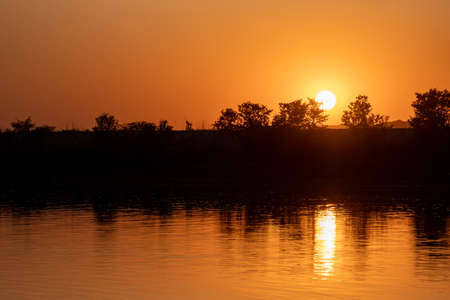 A breathtaking view of an orange sunrise with the sun's reflection in the waterの写真素材