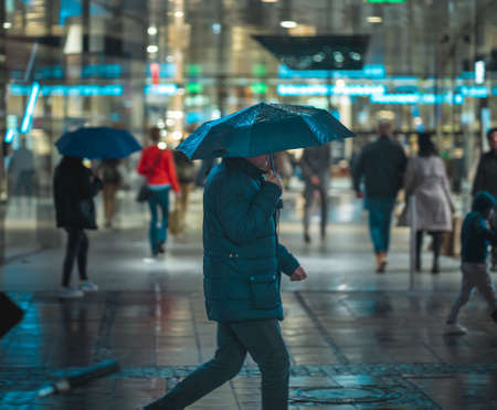 MUNICH, GERMANY - Feb 01, 2020: People crossing the street during a wet rainy night in Munich. Neon lights illuminating the scene. City traffic in the background.の写真素材