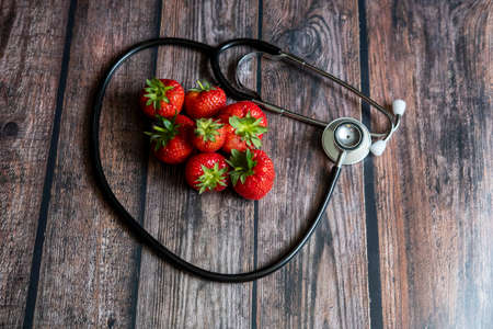 Stethoscope with strawberries and black seedless grape on top of wooden table. Medical and healthcare conceptual.の写真素材