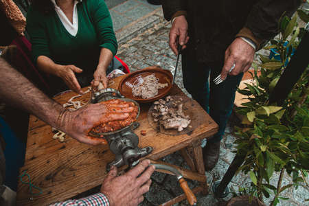 A group of people grinding meat with an old fashioned grinder and preparing a kielbasa in outdoors