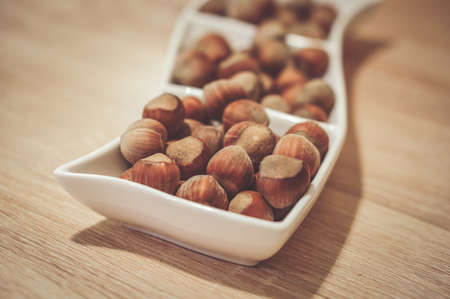 a soft focus shot of fresh whole hazelnuts on a white serving dishの写真素材