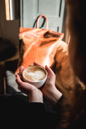 A vertical shot of a woman holding a cup of hot cappuccinoの写真素材