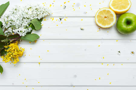 A high angle shot of beautiful flower petals, green apple and a slice of citrus fruit in a white wooden tableの写真素材