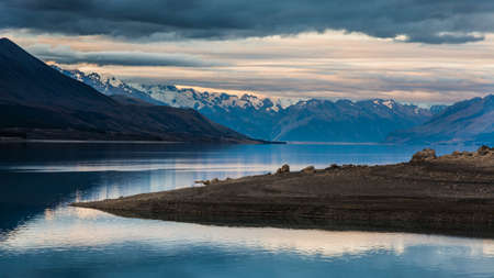 A beautiful shot of a lake with mountains in the distance under a cloudy skyの写真素材