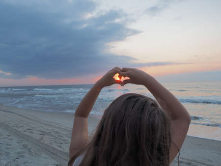 A little girl forming a heart with hands on the beach surrounded by the sea during the sunsetの写真素材