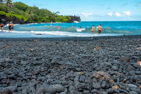 A beach with black stones and many people swimming