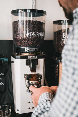 A vertical shot of a man grinding coffee beans with a machineの写真素材