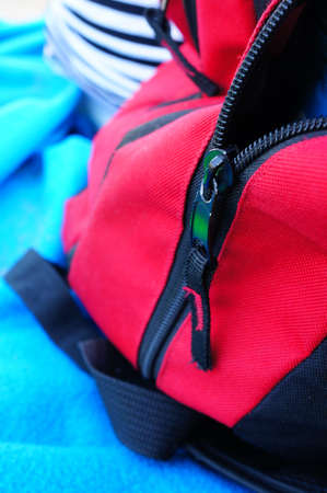 A closeup of a black and red zipper on a backpack under the sunlight with a blurry backgroundの写真素材