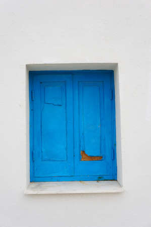 A vertical shot of an old window with blue shutters on a white wall