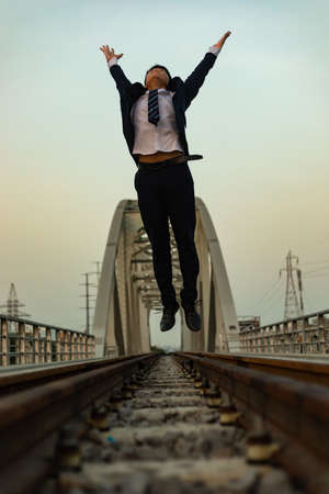 A low angle shot of a young Asian man in a suit jumping for success with hands lifted high