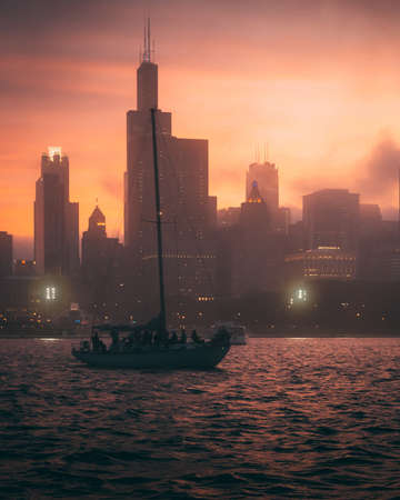 The mesmerizing view of the boat in the ocean and the silhouettes of high buildings during sunsetの写真素材