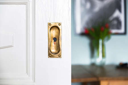 A closeup shot of a white wooden door with a rusty keyhole on a blurred background