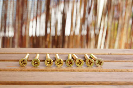 A closeup shot of a row of screws laid on a wooden tableの写真素材