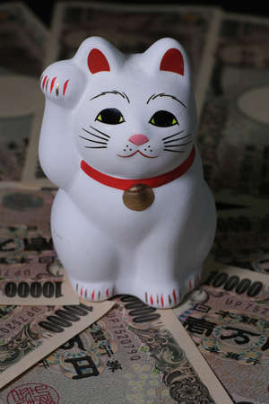 A vertical closeup shot of a Japanese lucky cat (Maneki-neko)  on Japanese 10000 banknotes