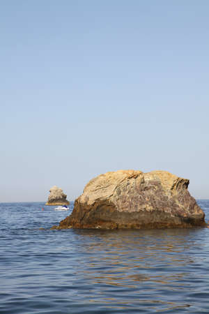 A vertical shot of a rock in the ocean under a blue sky