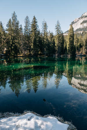 A vertical picture of a lake surrounded by rocks and forests with trees reflecting on the waterの写真素材