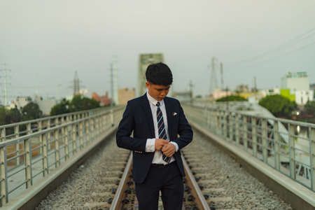A young Asian businessman standing in the middle of a railway fixing his cuffの写真素材