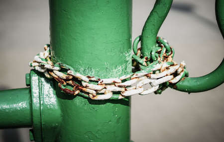 A closeup of an old rusty chain around a green pipe under the lights with a blurred backgroundの写真素材