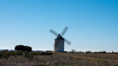 A picture of a lonely typical spanish windmill in a field under a blue skyの写真素材