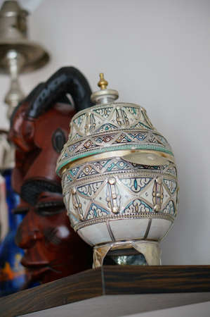 A beautiful shot of an antique vase on a wooden shelf in front of a white wallの写真素材