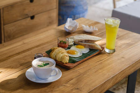 A tray of food and cookies on a wooden table next to a glass of juice and coffeeの写真素材