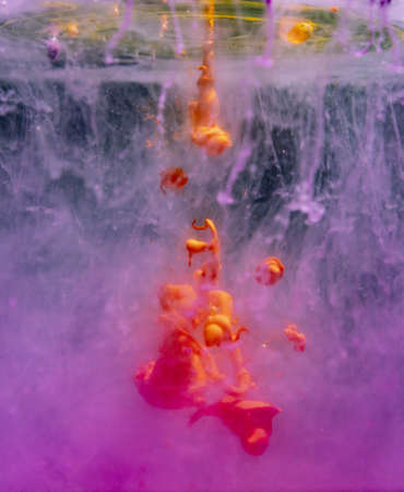 An orange-yellow acrylic paint drop with pink hazy backgroundの写真素材