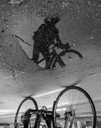 A greyscale of the reflection of a person with a bicycle on the wet asphalt after the rainの写真素材