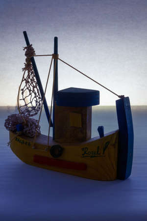 A vertical shot of a wooden ship toy placed on a blue surface with a light background