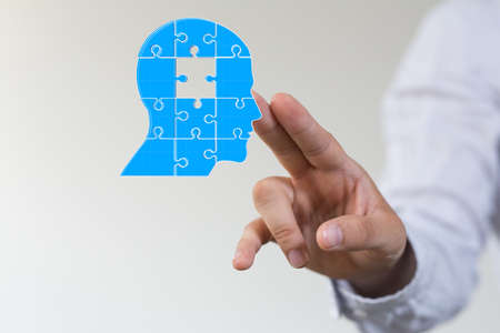 A head consisting of blue pieces of a jigsaw puzzle next to a person's fingersの写真素材